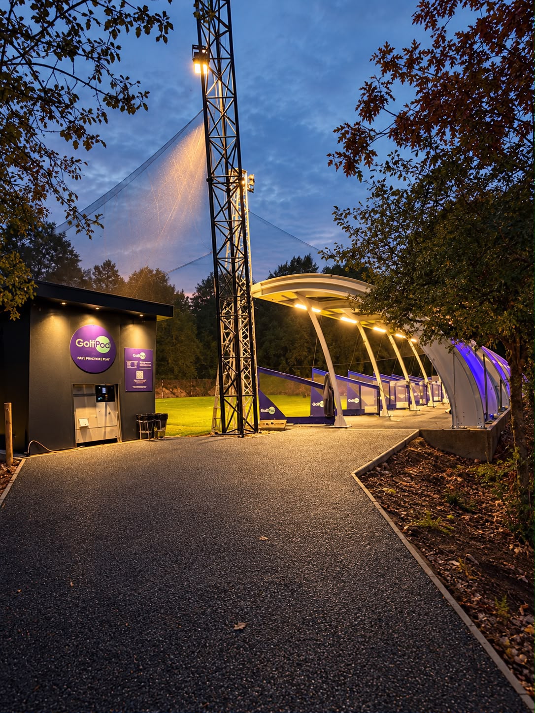 GolfPod covered driving range bays illuminated in the evening with outdoor golf practice facilities.
